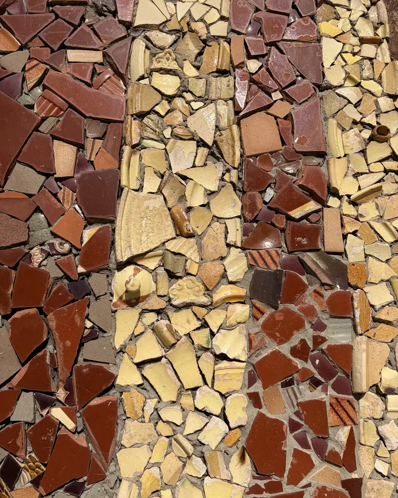 A wall mosaic made of broken ceramics in red, plum, ochre and cream, set in cement, in Saint-Quentin-la-Poterie