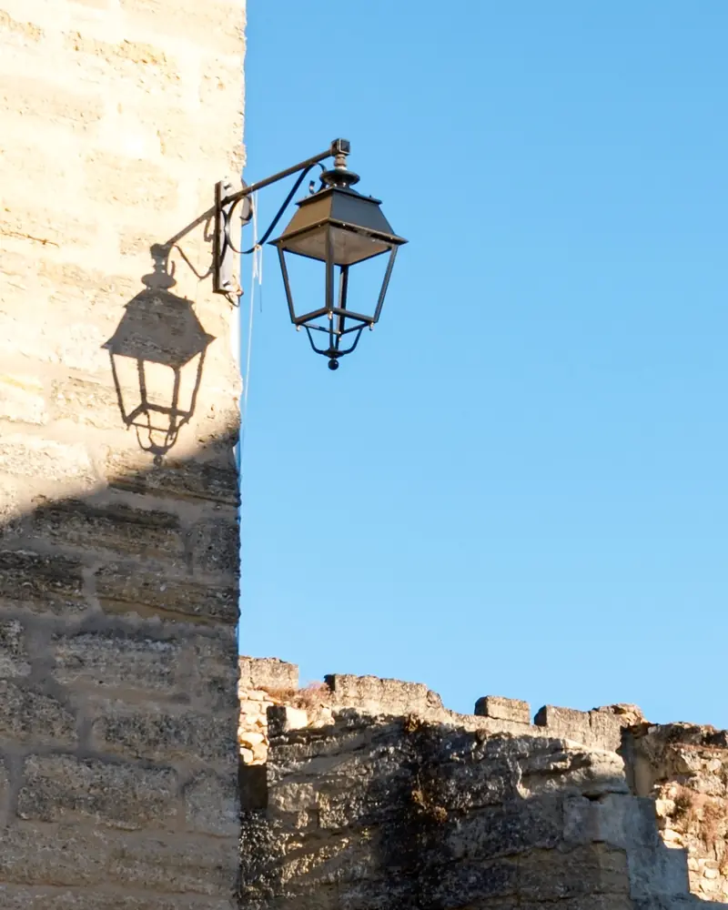 A wrought-iron lantern on a sandstone wall, casting its shadow, against a clear blue sky