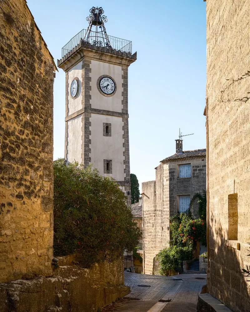 The clock tower of Saint-Siffret with an iron bell cage rising above golden stone lanes
