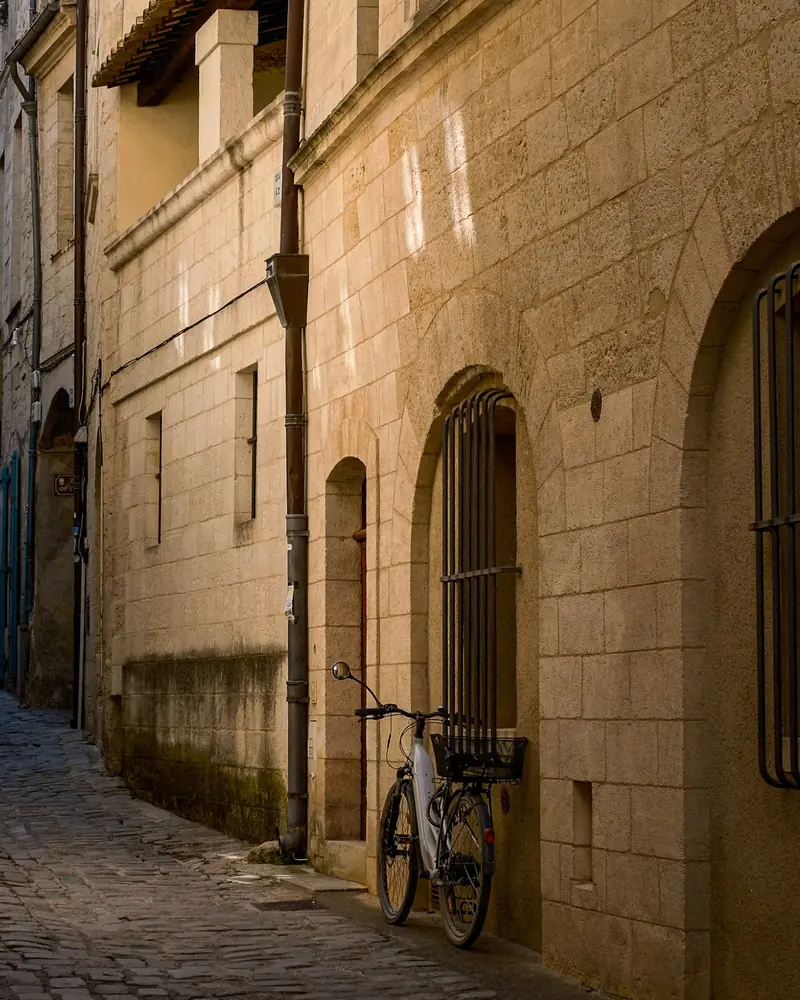 A bicycle leaning against a golden stone wall in a quiet cobbled lane in Uzès